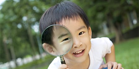 Petit garçon asiatique dans un parc regardant à travers une loupe