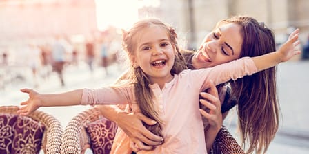 Nounou étudiante dans un café avec sur ses genoux une petite fille ouvrant les bras