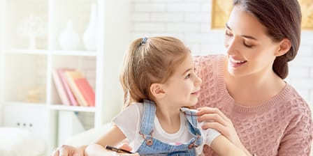Nounou souriante tenant une petite fille sur ses genoux en intérieur