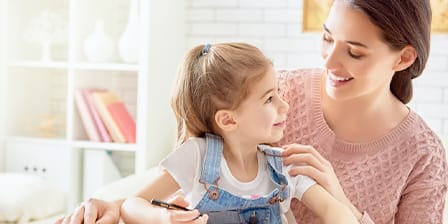 Nounou souriante tenant une petite fille sur ses genoux en intérieur