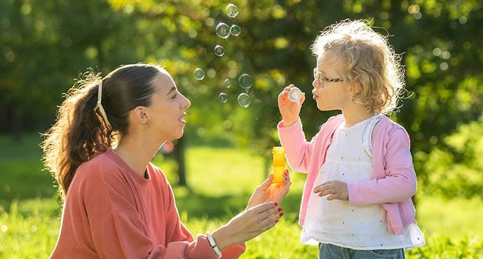 Nounou dans un parc avec un enfant qui fait des bulles 