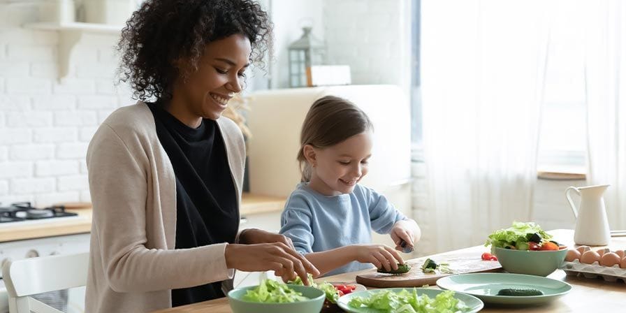 Petite fille préparant une salade avec sa nounou métisse