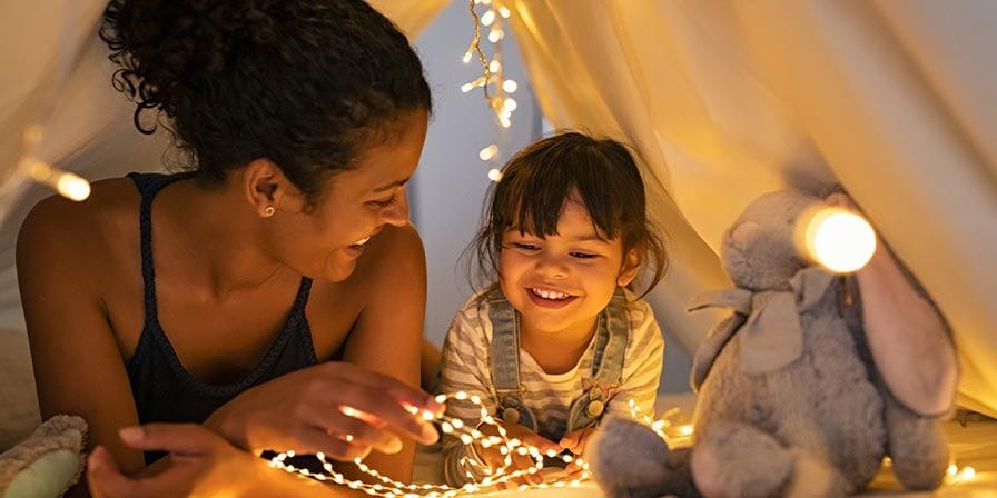 Petite fille et nounou sous une tente en intérieur avec des guirlandes lumineuses
