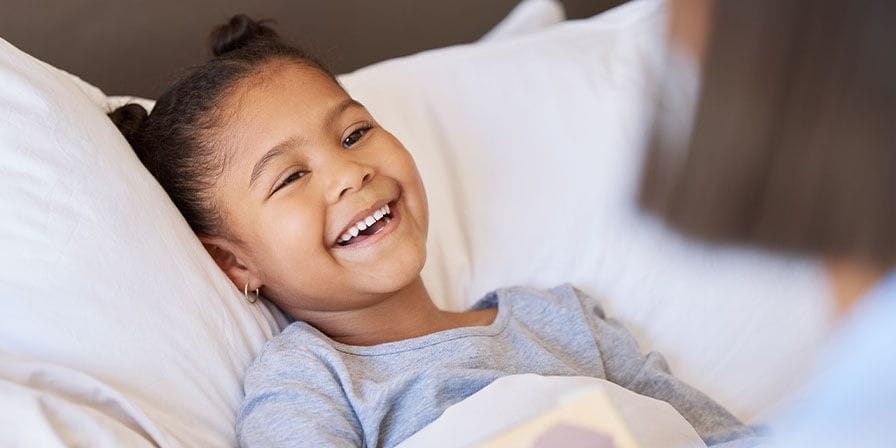 Petite fille métisse qui sourit dans son lit avec sa nounou près du lit