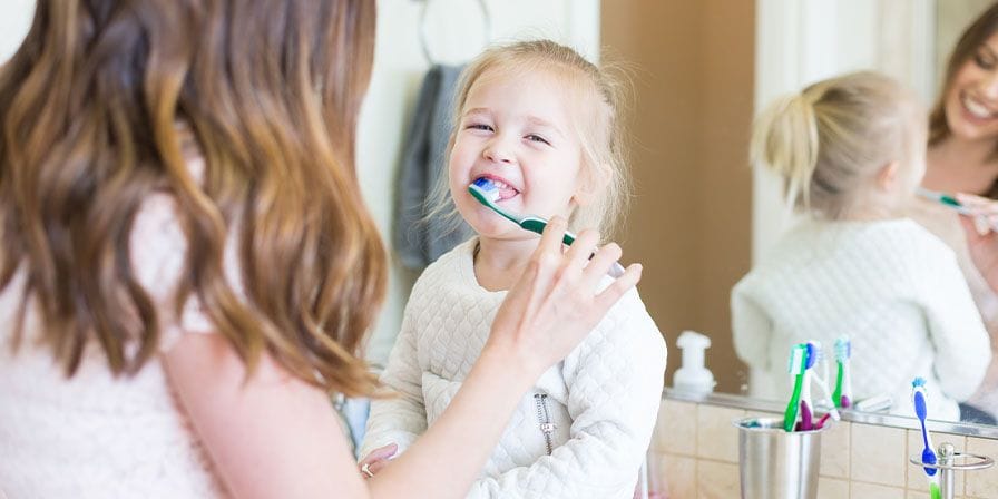 Une nounou qui brosse les dents d'une petite fille