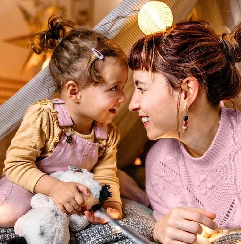 Moment complice entre une petite fille et sa nounou sous une tente dans le salon