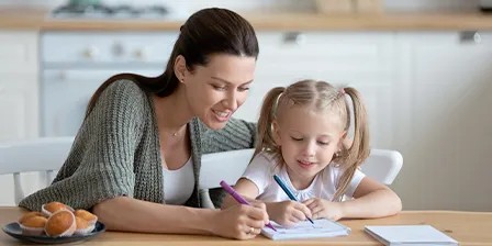 Nounou en train de superviser une petite fille qui écrit dans une cuisine