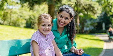 Nounou étudiante assise sur un banc dans un parc à côté d'une petite fille souriante