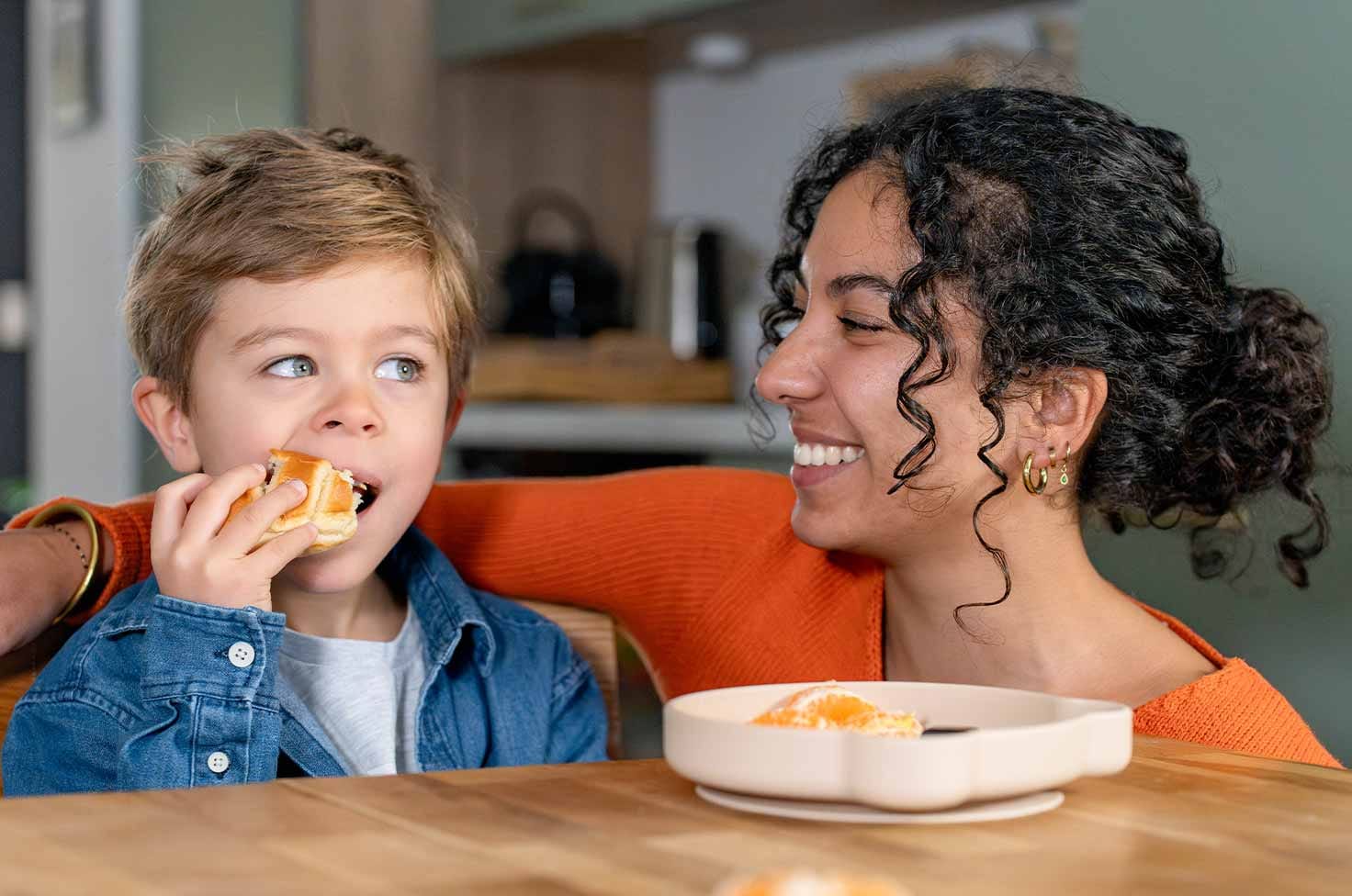 Nounou étudiante partageant un goûter avec un petit garçon mangeant une viennoiserie