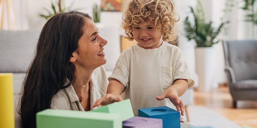 Petit garçon aux cheveux bouclés jouant avec des cubes aux côtés de sa nounou