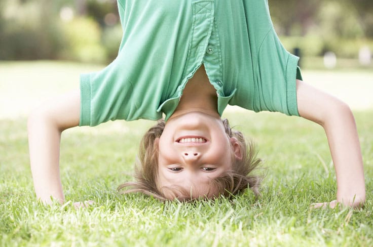 Petit garçon souriant qui fait le poirier sur l'herbe