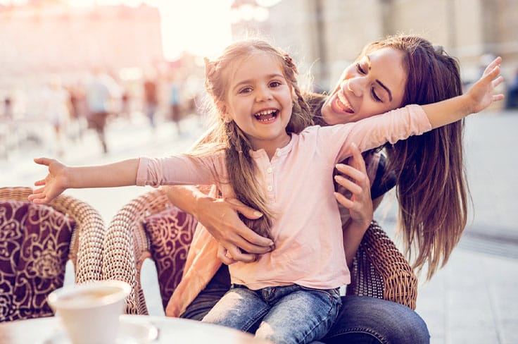 Nounou étudiante dans un café avec sur ses genoux une petite fille ouvrant les bras
