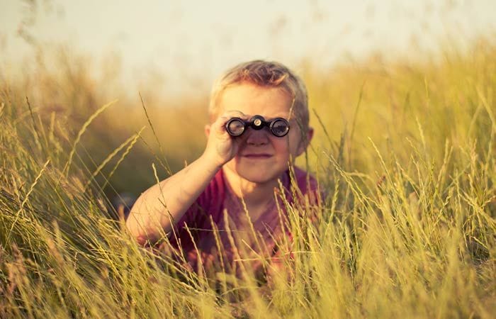 Petit garçon regardant à travers des jumelles dans un champ d'herbes hautes